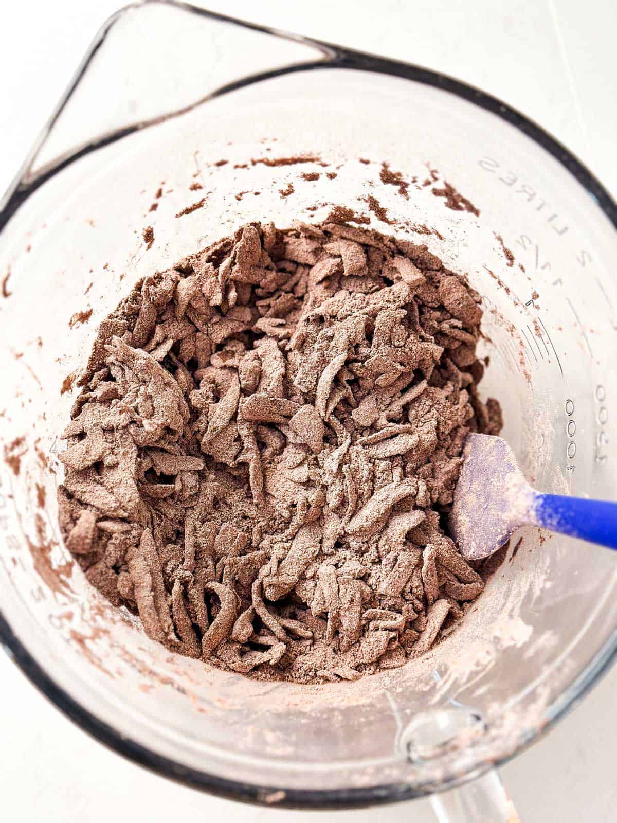 raw shredded zucchini  combined with dry ingredients for chocolate zucchini bread in glass bowl