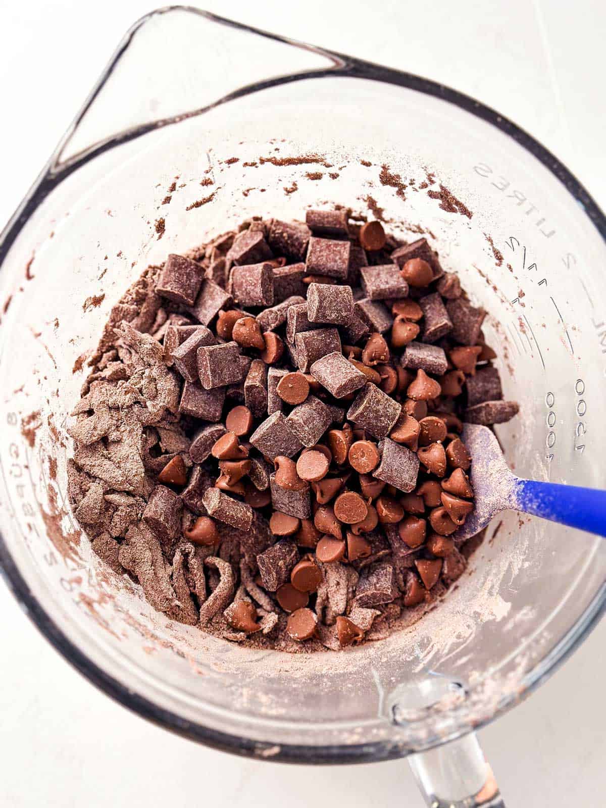 chocolate chips and chocolate chunks on top of dry ingredients for chocolate zucchini bread in glass bowl