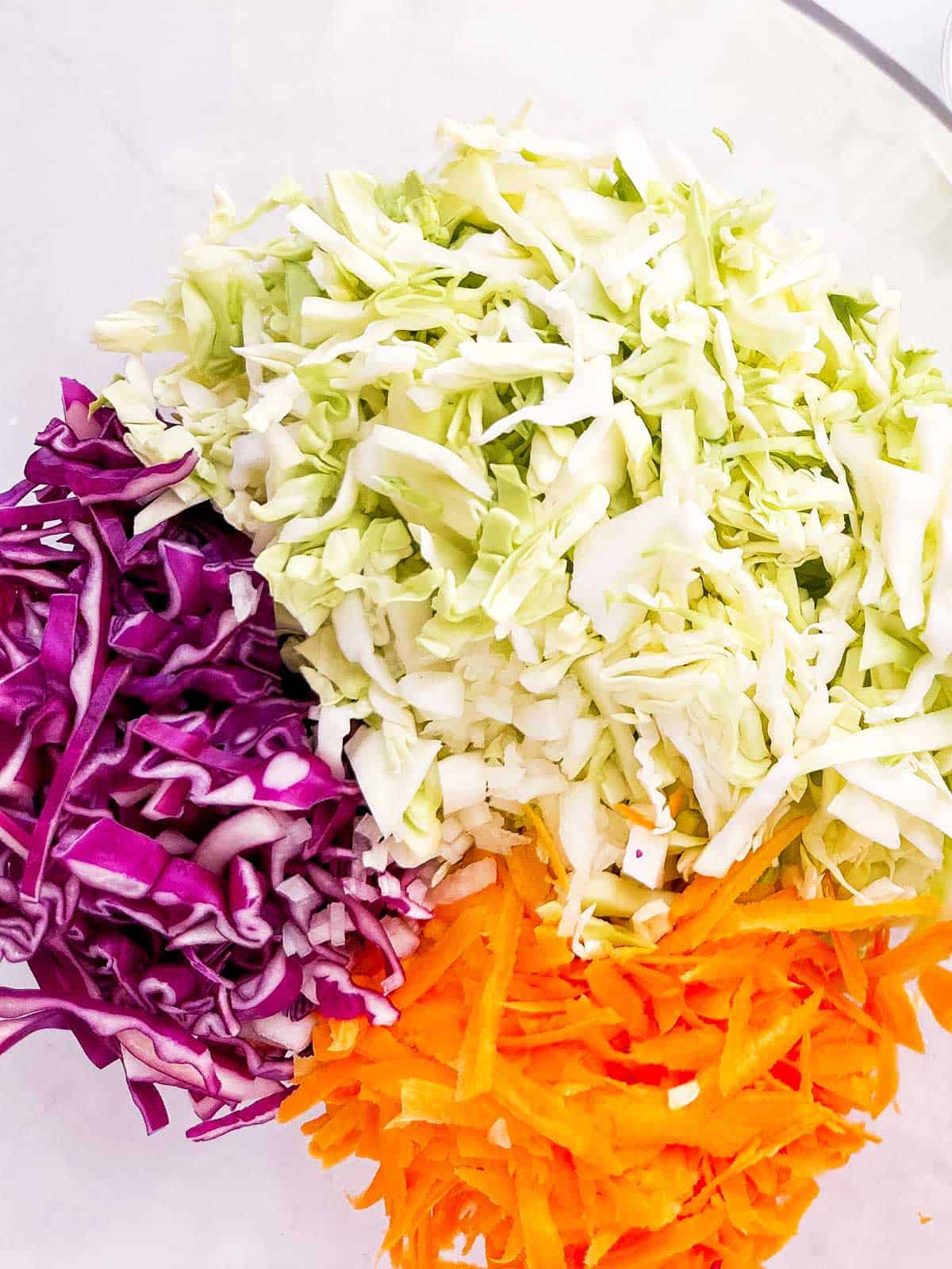 overhead view of shredded green and purple cabbage in glass bowl with shredded carrot