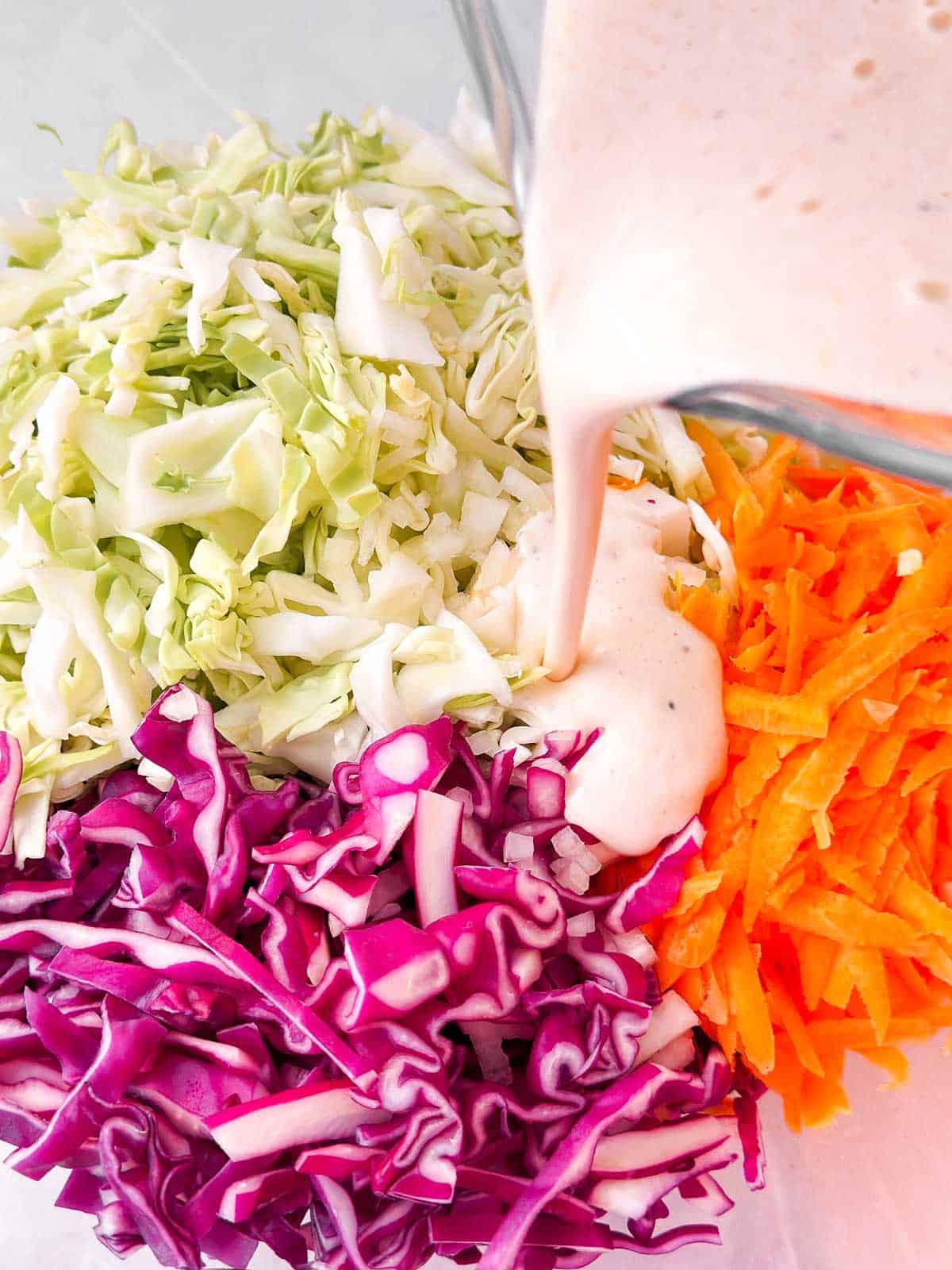 dressing pouring from glass measuring jug over shredded cabbage and carrots