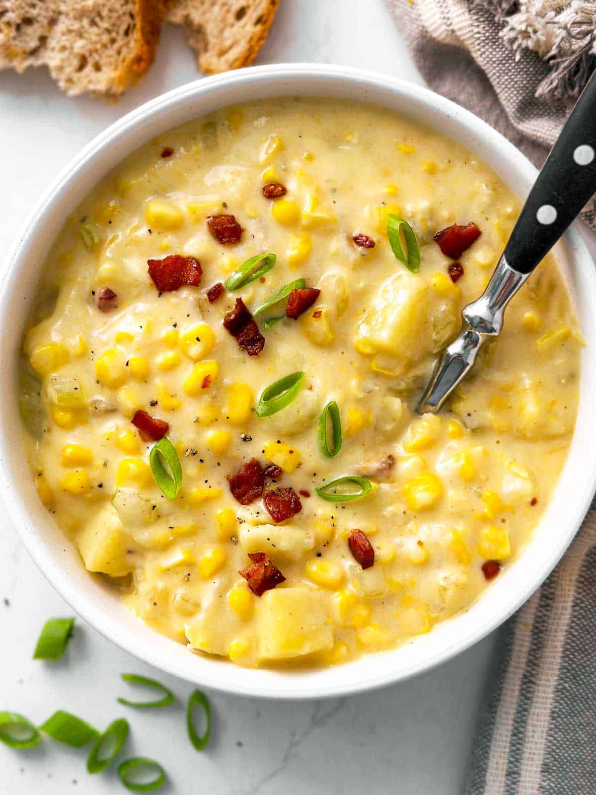 overhead view of corn chowder in white bowl with spoon stuck in