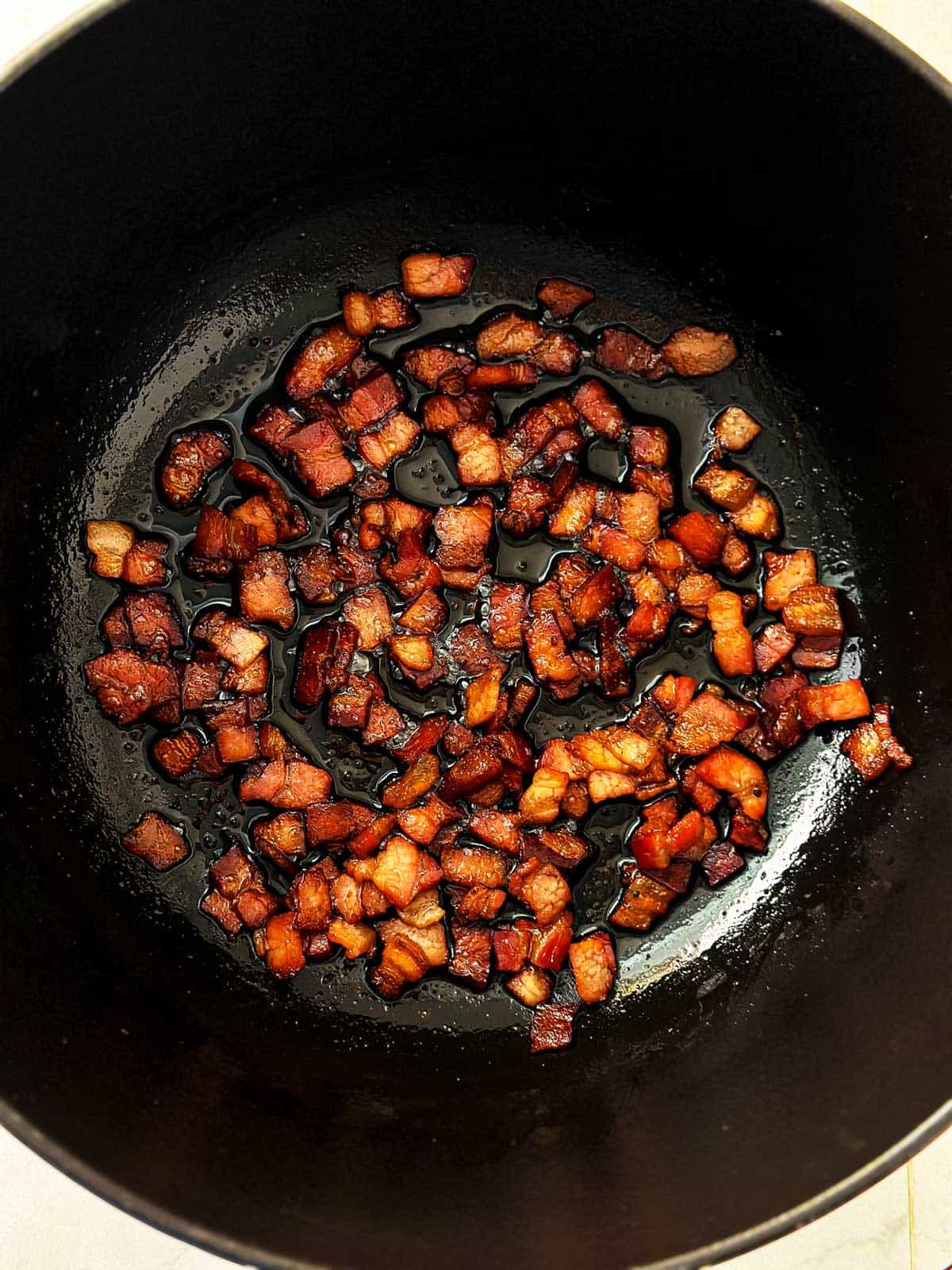 overhead view of crispy browned bacon pieces in black Dutch oven