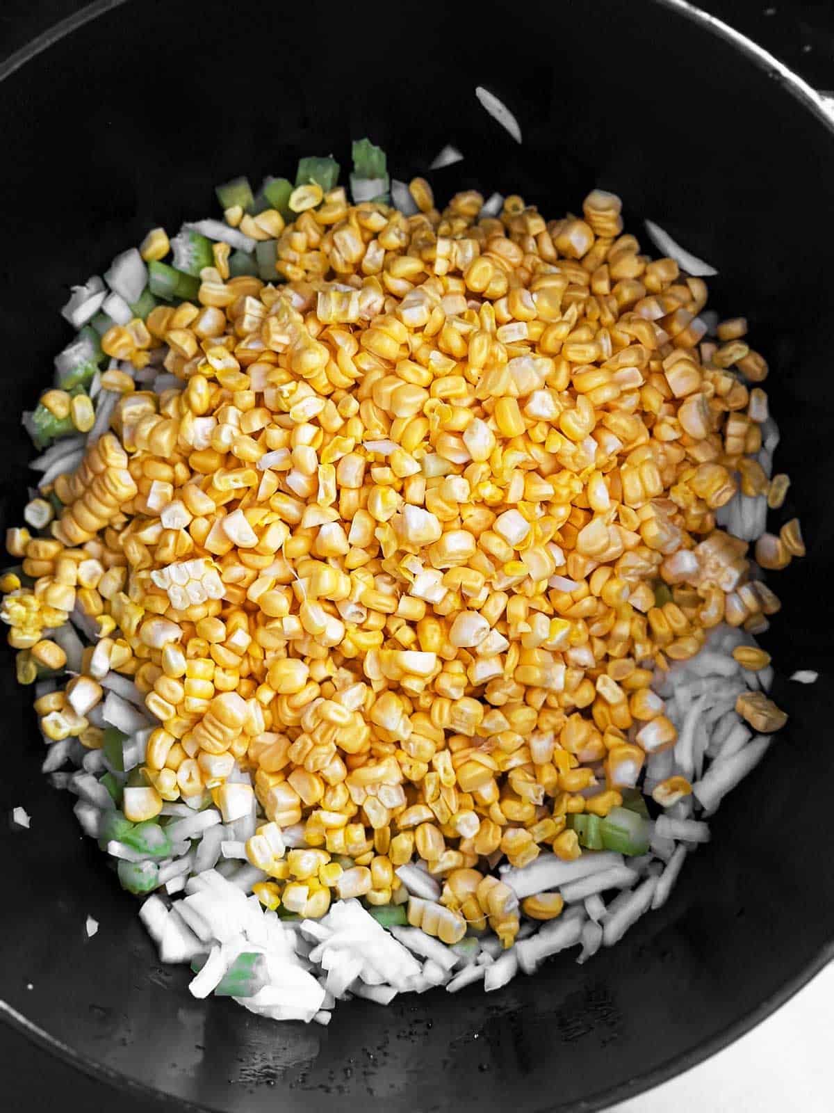 overhead view of raw corn, onion and celery in black Dutch oven