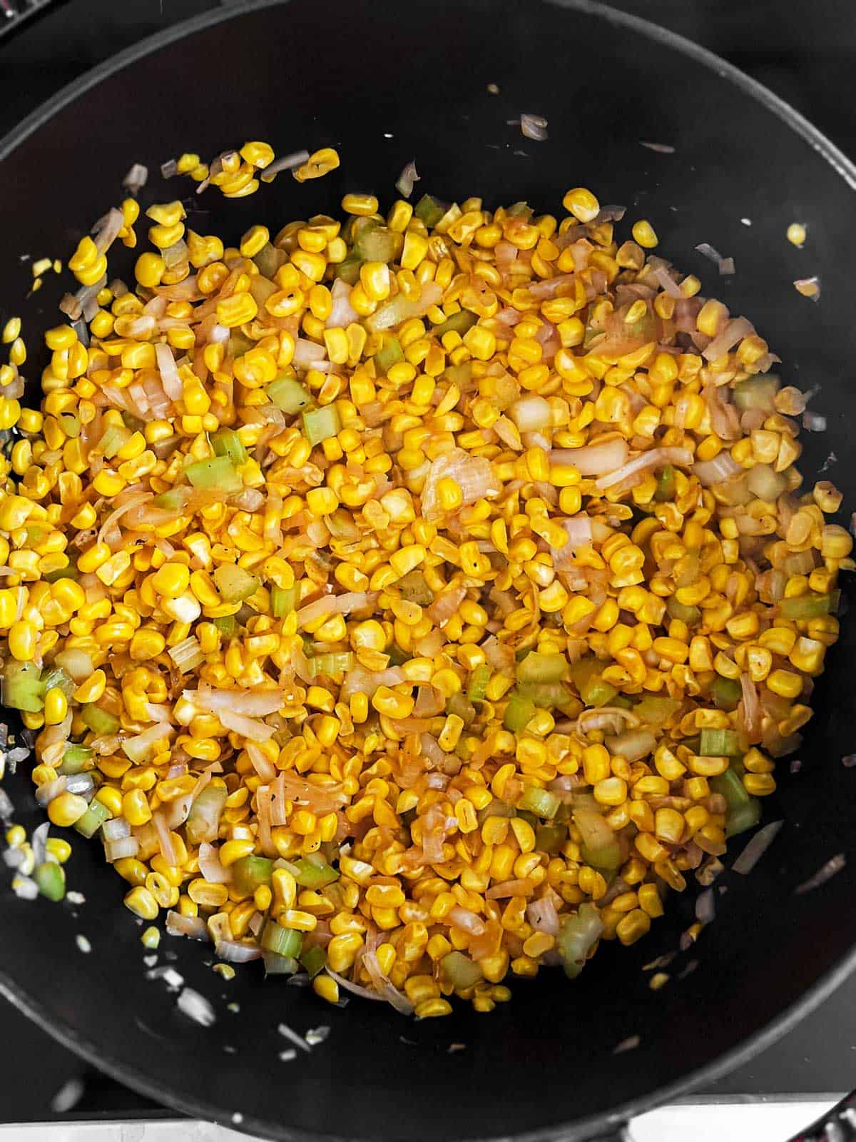 overhead view of cooked corn, onion and celery in black Dutch oven