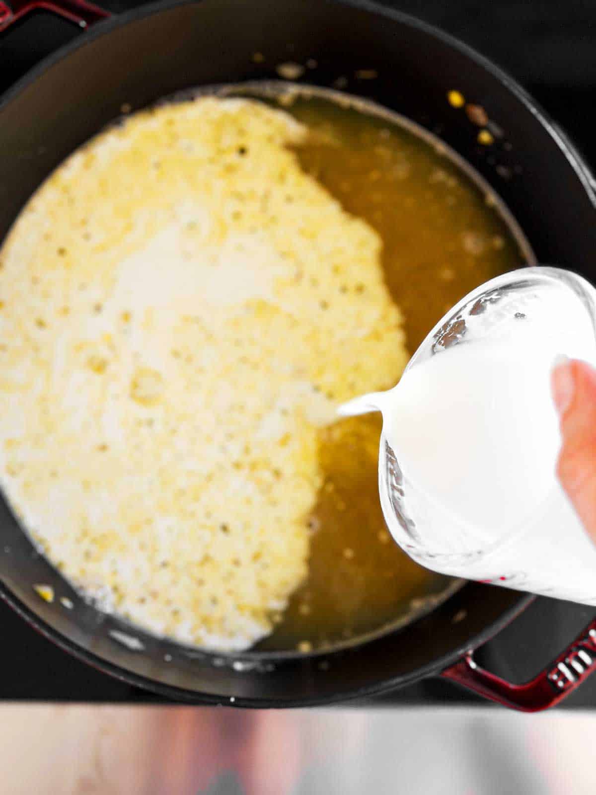 overhead view of female hand pouring cream into Dutch oven