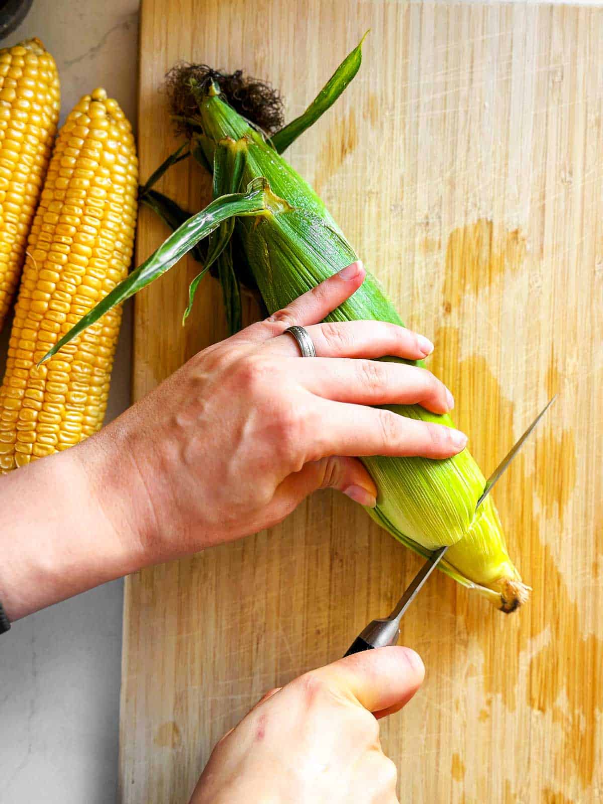 overhead view of female hands cutting off end of corn ear