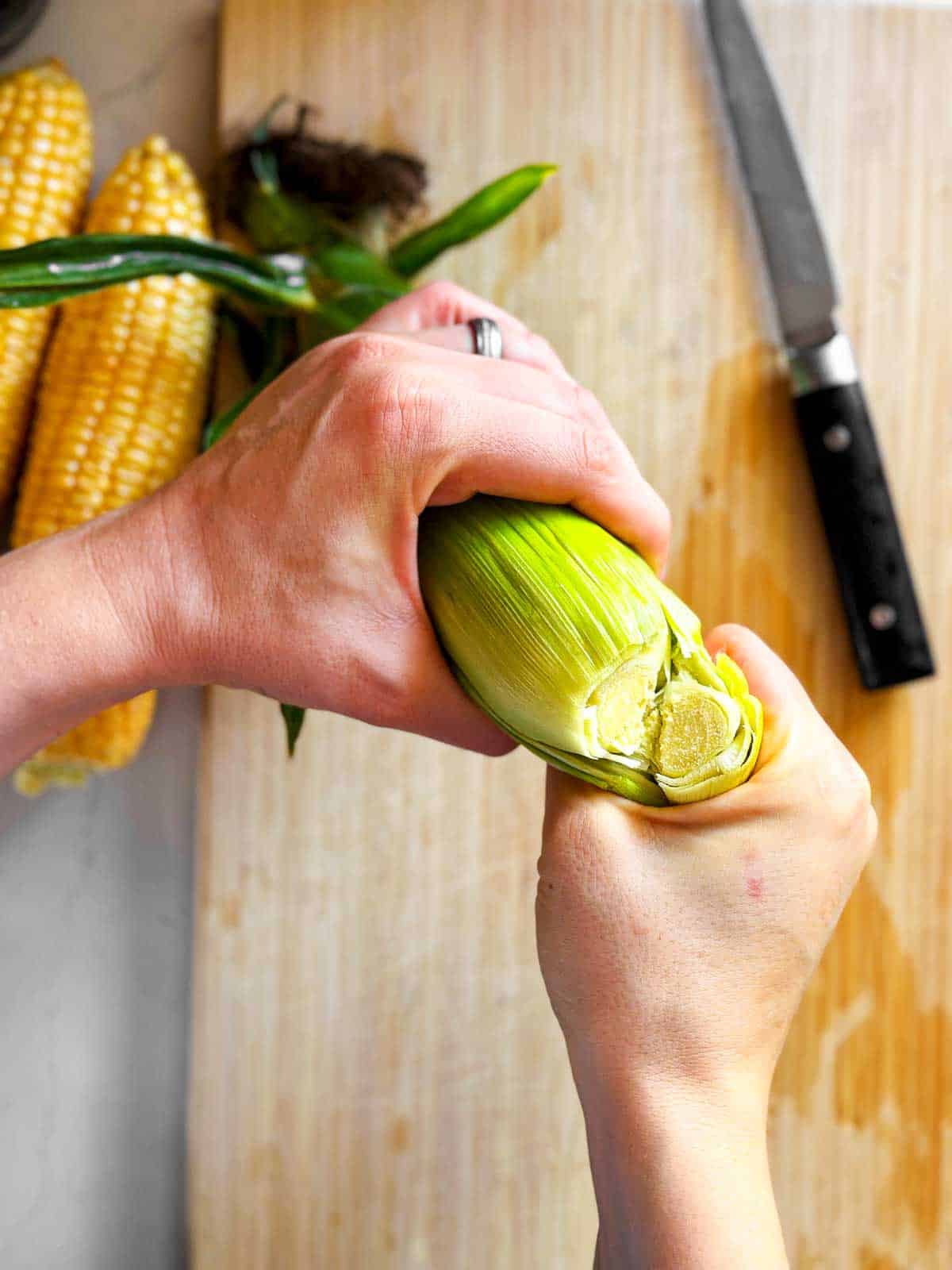 female hands breaking off end of unshucked corn ear