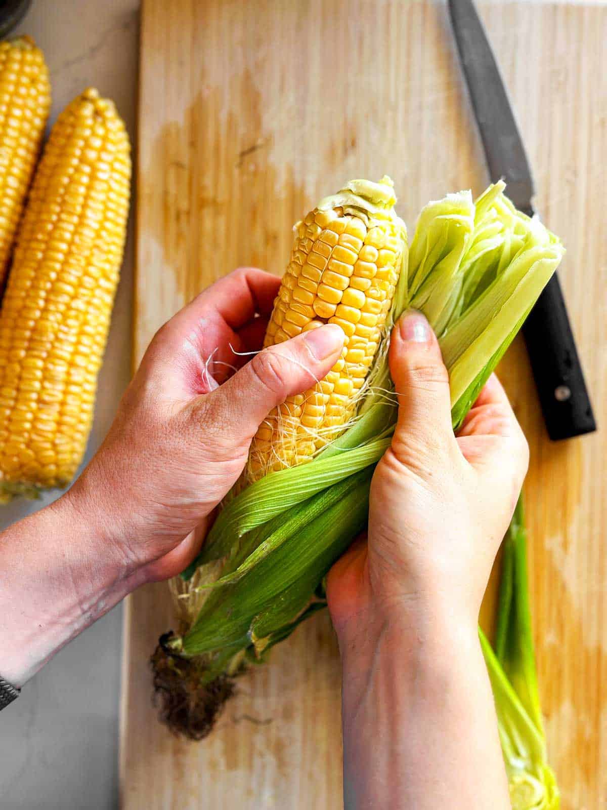 female hands shucking cob of corn