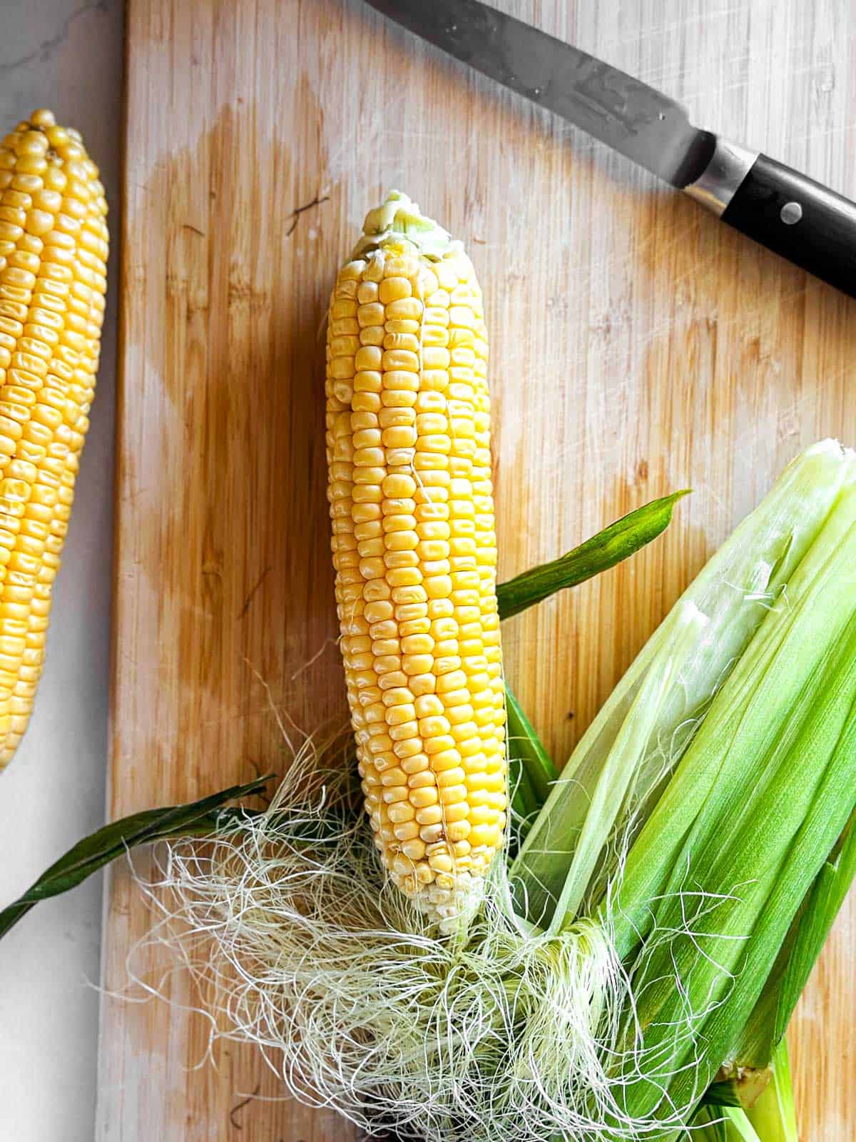 overhead view of shucked corn ear on wooden cutting board