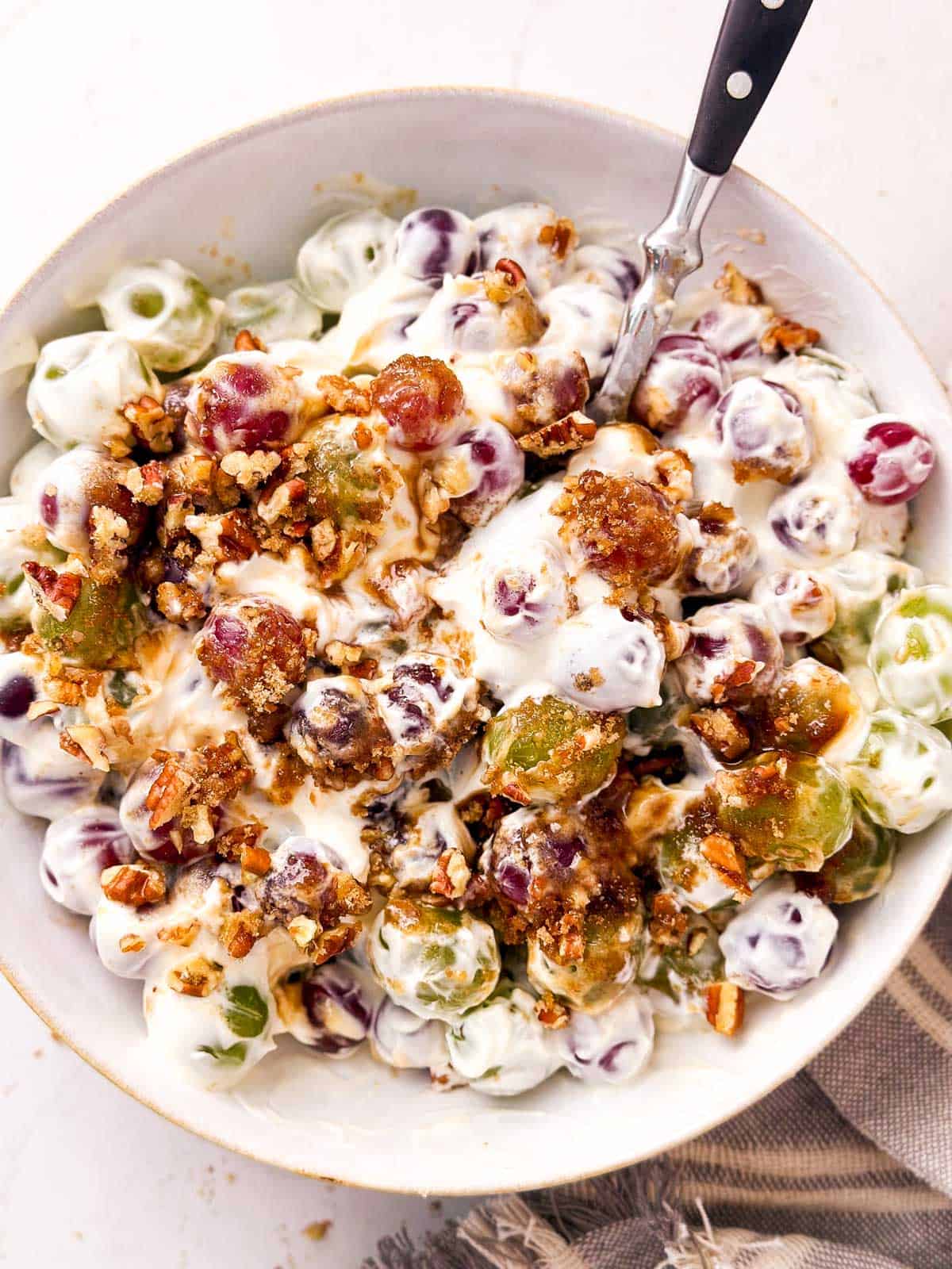 overhead view of grape salad in white bowl with spoon stirring