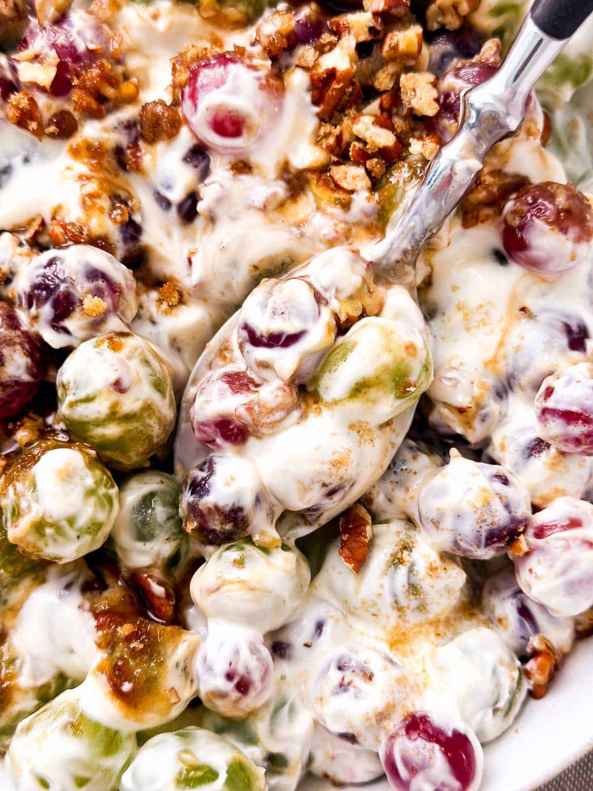 overhead close up view of spoon scooping creamy grape salad