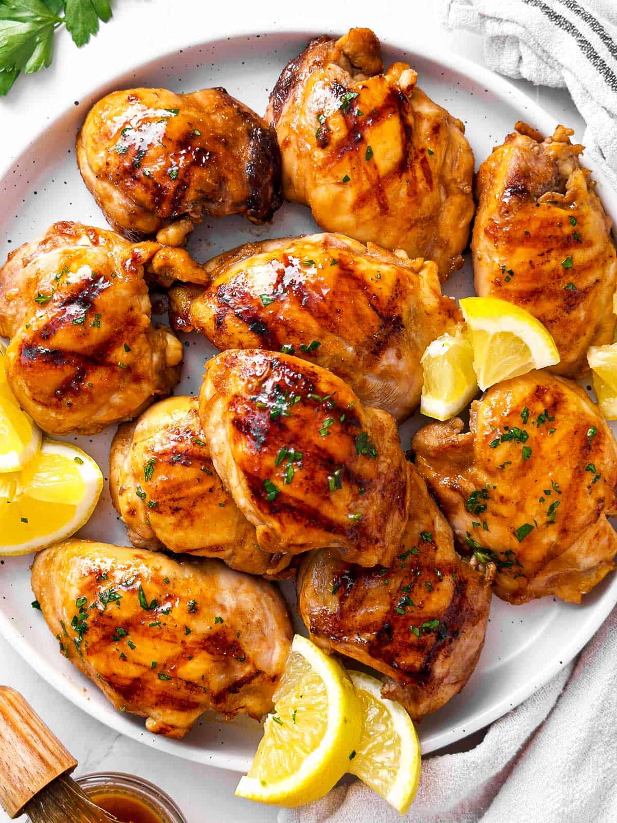 overhead view of grilled chicken thighs on white plate with lemon wedges