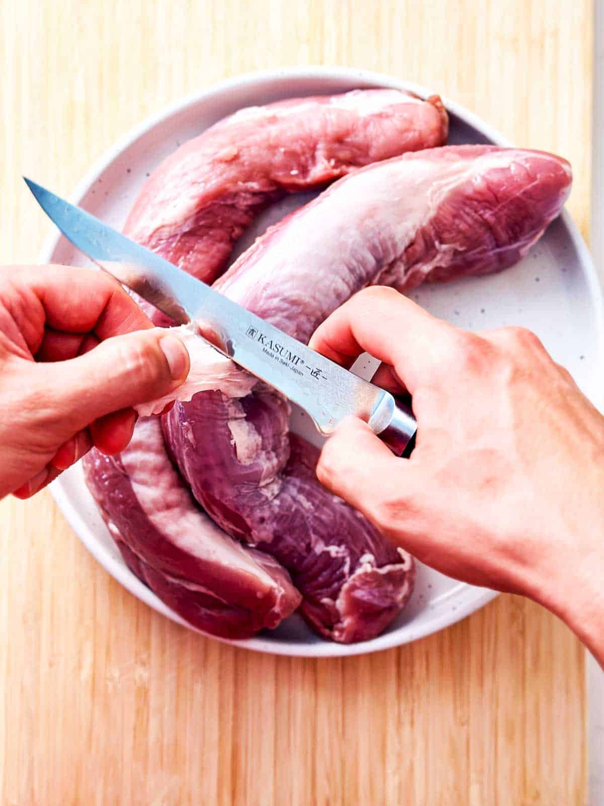 overhead view of male hands slicing silver skin off of pork tenderloin