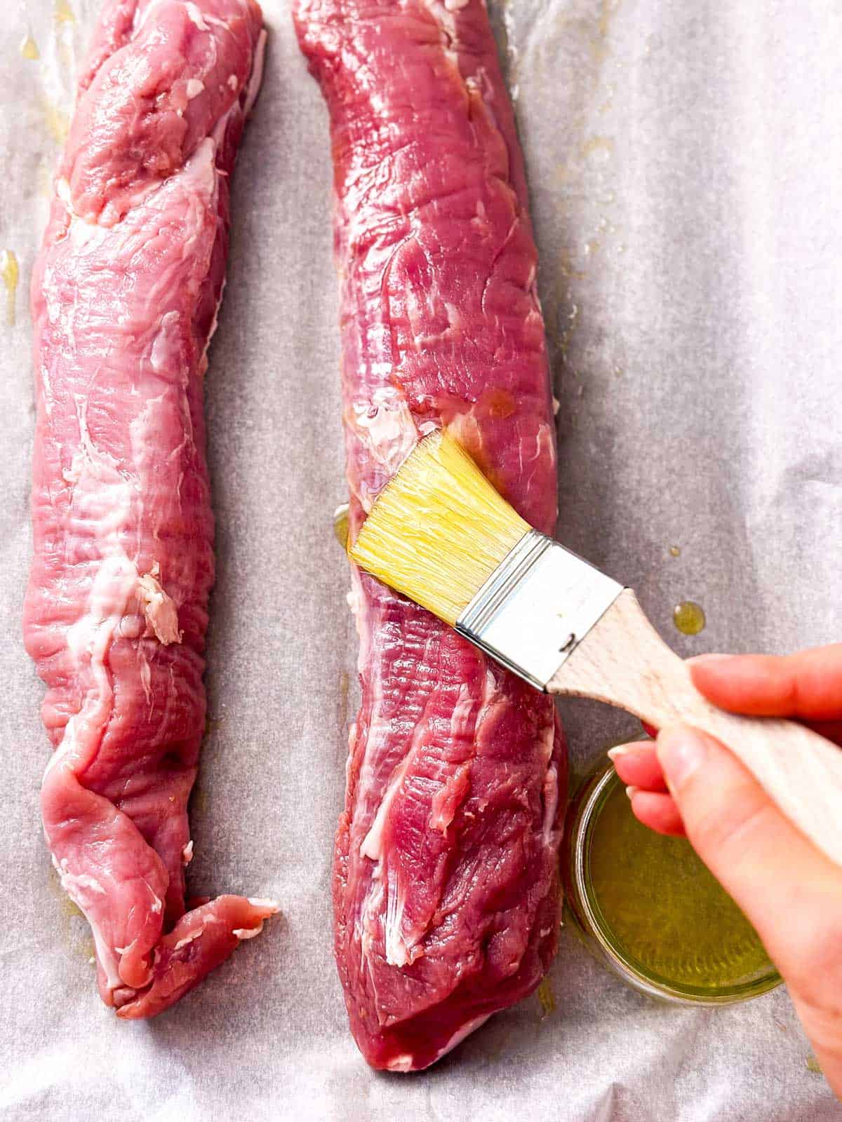 overhead view of female hand brushing pork tenderloin with oil