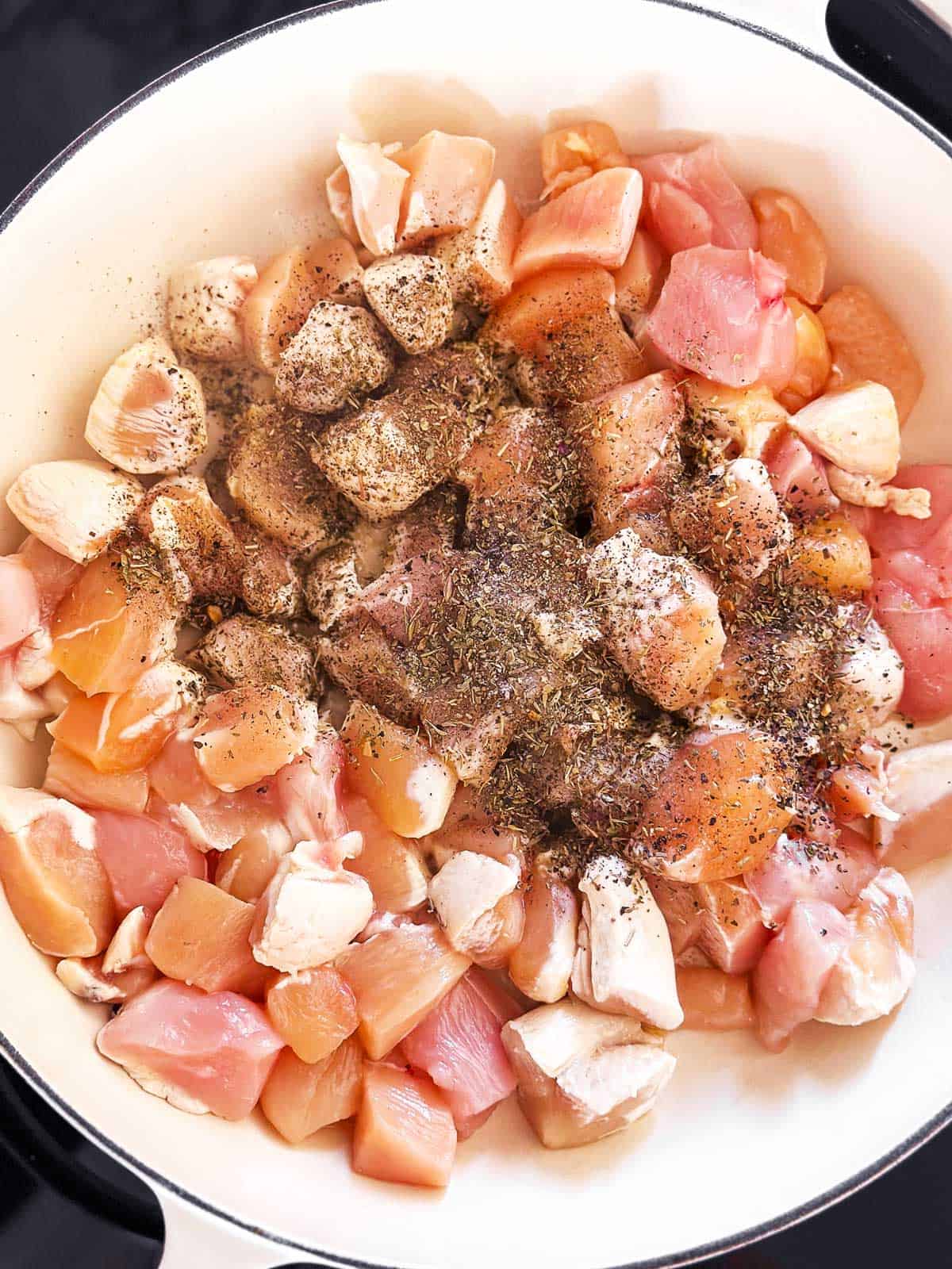 overhead view of raw diced chicken breast in skillet with seasoning