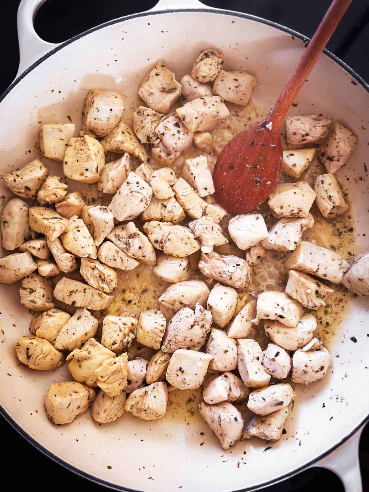 overhead view of browned diced chicken breast in skillet with seasoning