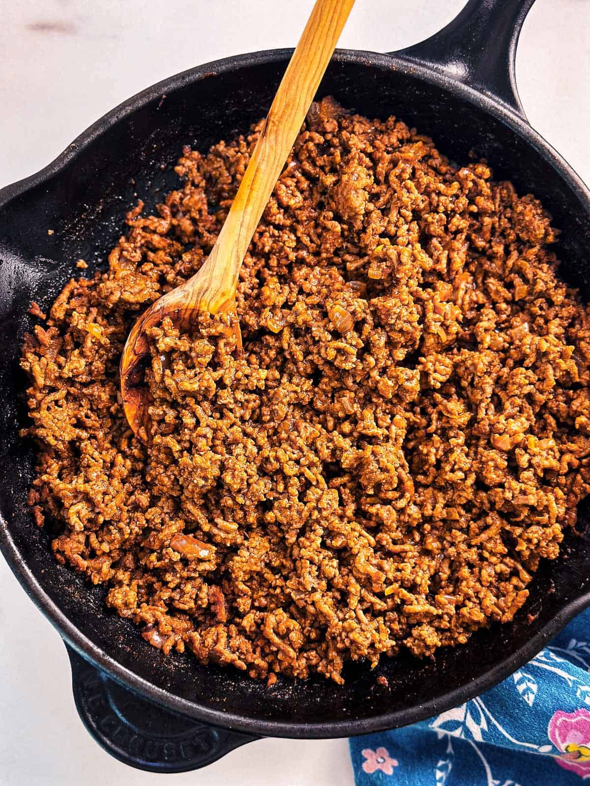 overhead view of taco meat in black skillet with wooden spoon stuck in