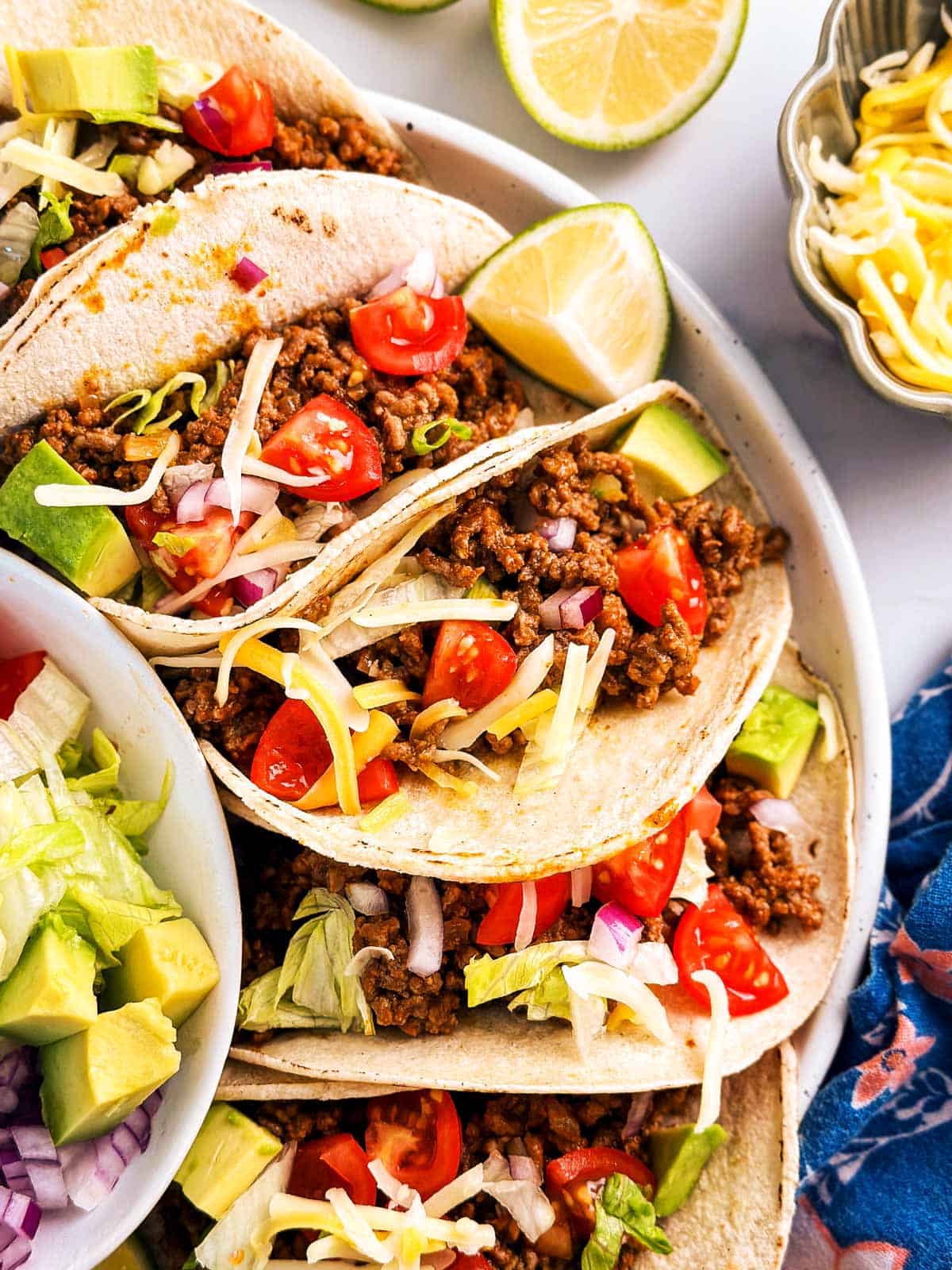 overhead view of several ground beef tacos on white plate surrounded by taco toppings