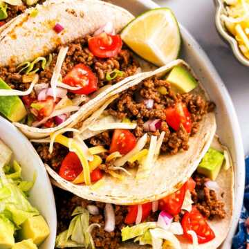 overhead view of several ground beef tacos on white plate surrounded by taco toppings