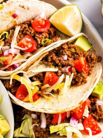 overhead view of several ground beef tacos on white plate surrounded by taco toppings