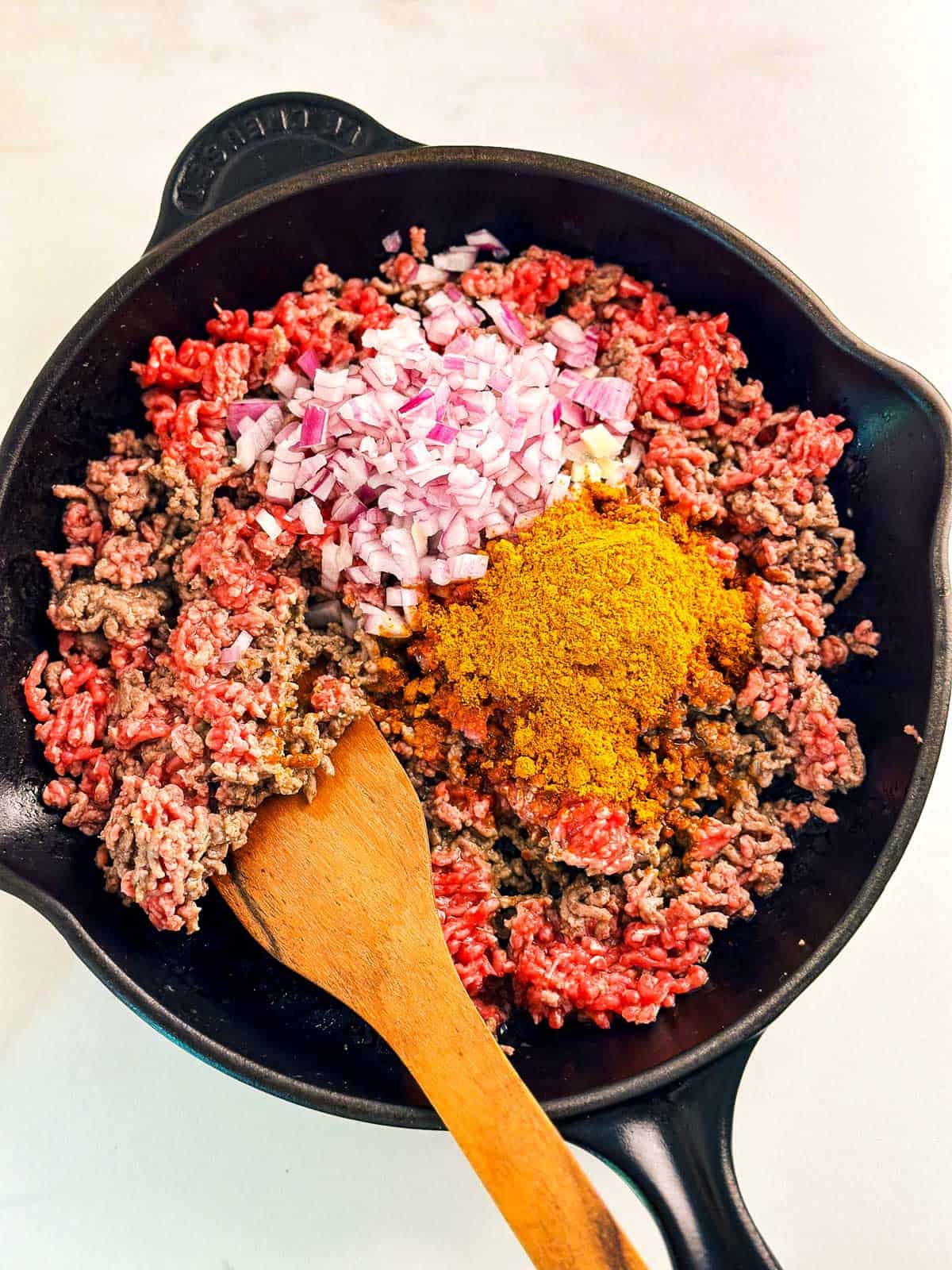 overhead view of raw ground beef in skillet with raw onion and spices