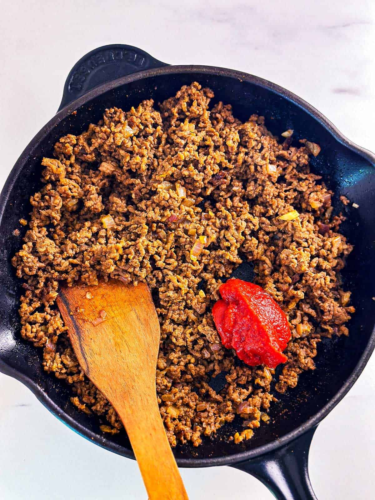 overhead view of cooked ground beef in skillet with tomato paste