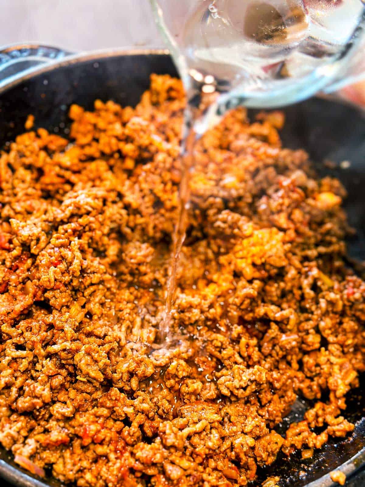 water pouring from glass measuring jug over browned ground beef