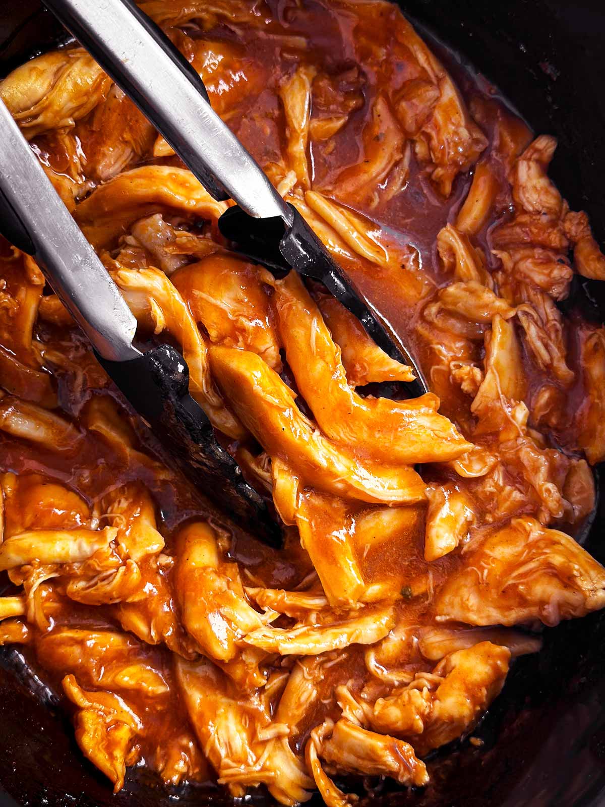 overhead close up view of bbq pulled chicken in crock with tongs