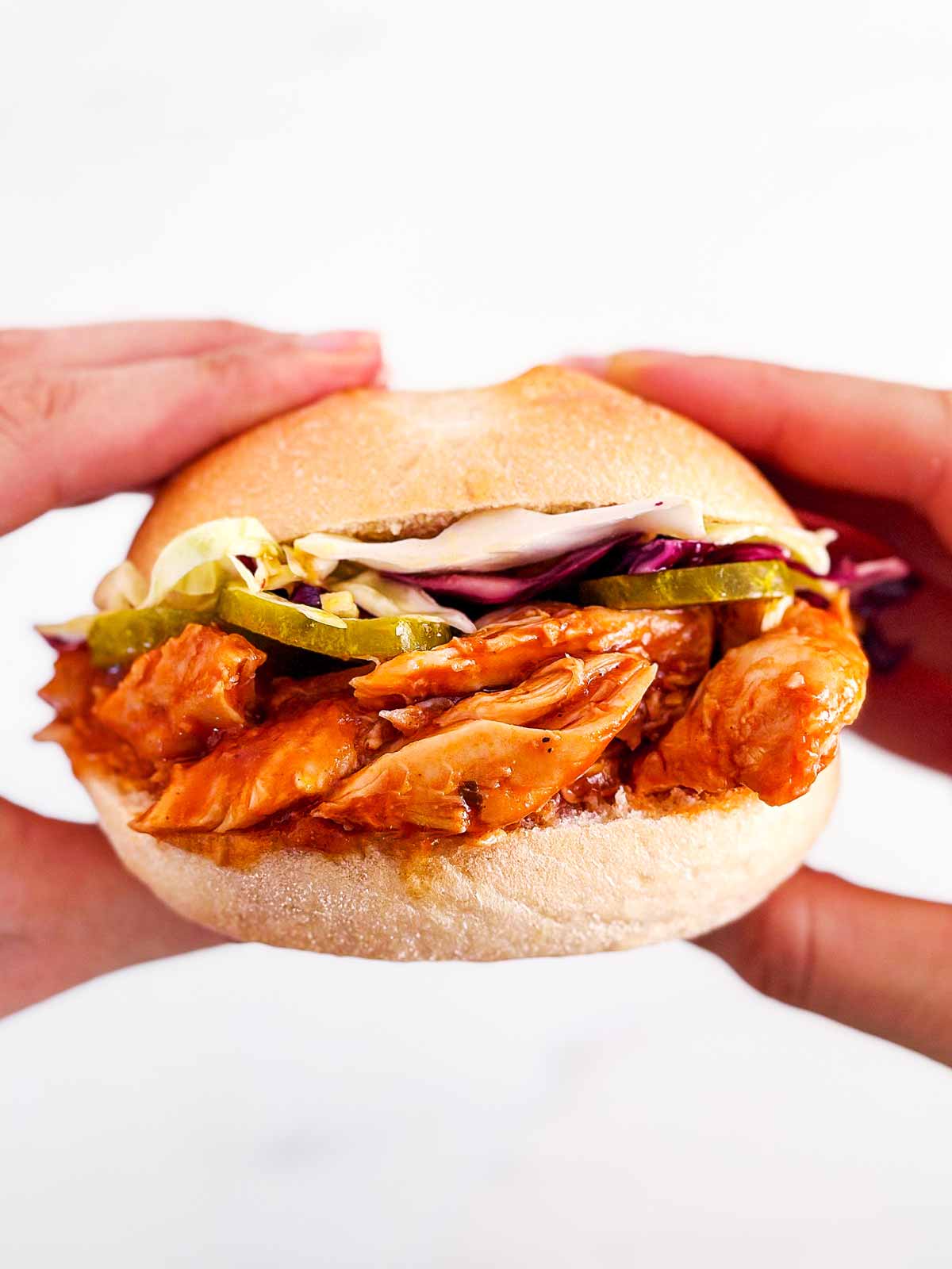 overhead view of female hands holding a pulled chicken sandwich