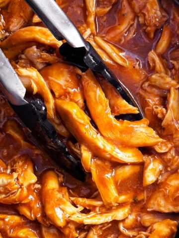 overhead close up view of bbq pulled chicken in crock with tongs