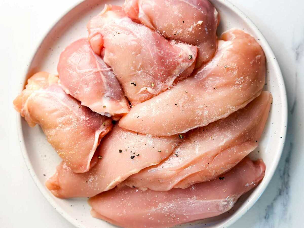 overhead view of seasoned raw chicken pieces on white plate