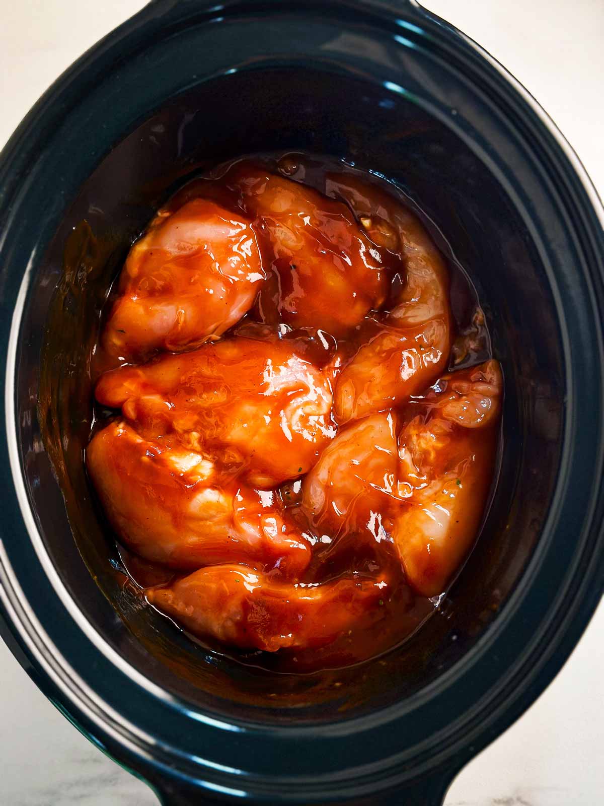 overhead view of uncooked bbq chicken in slow cooker