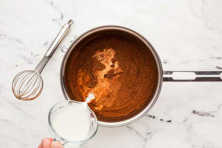 female hand pouring milk into saucepan with cocoa powder