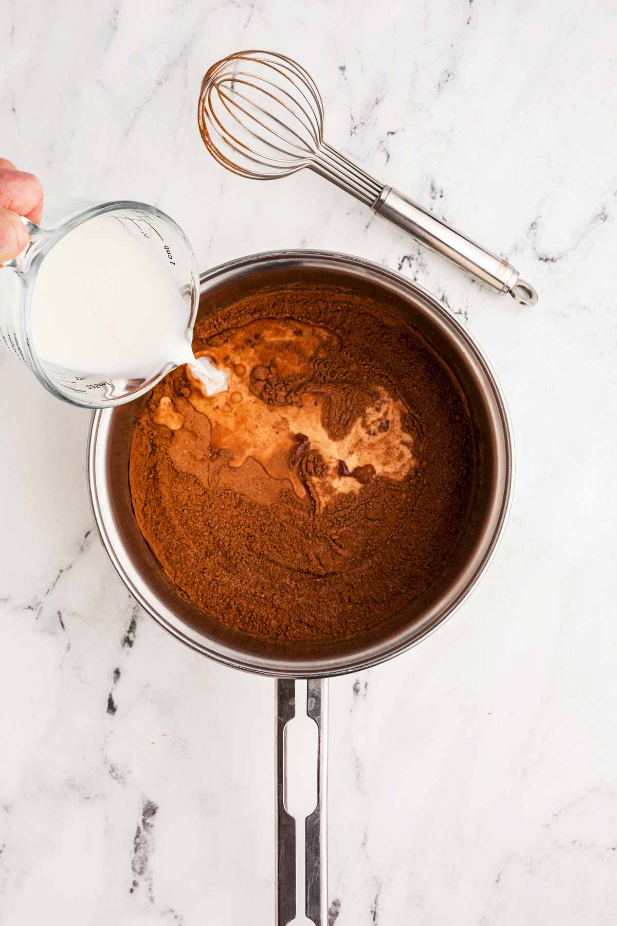 female hand pouring milk into saucepan with cocoa powder