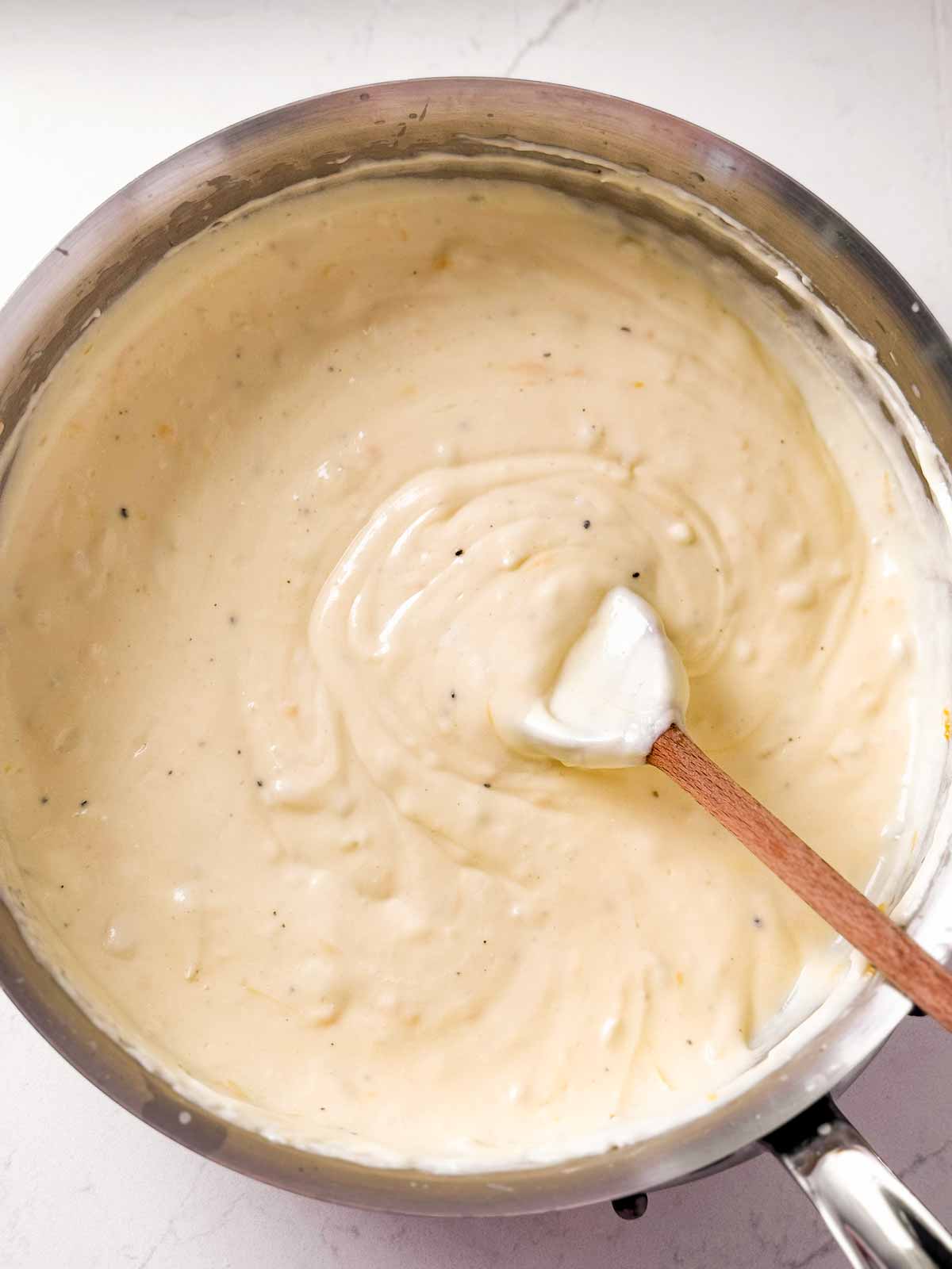 overhead view of cheese sauce in saucepan with wooden spoon