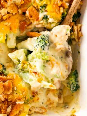 frontal close up view of wooden spoon scooping up broccoli cheese casserole from a white baking dish