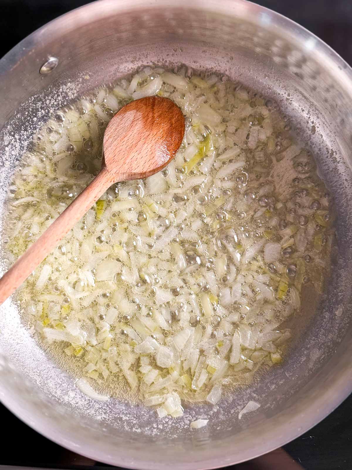 overhead view of cooked onion in saucepan with wooden spoon