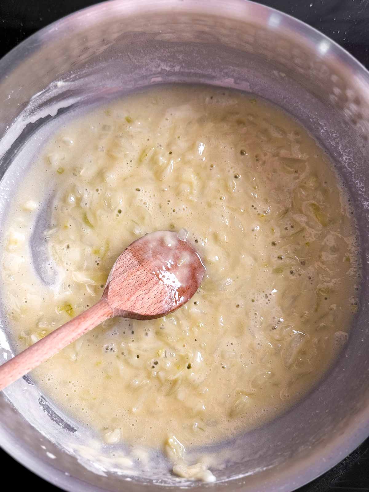 overhead view of cooked onion and flour roux in saucepan with wooden spoon