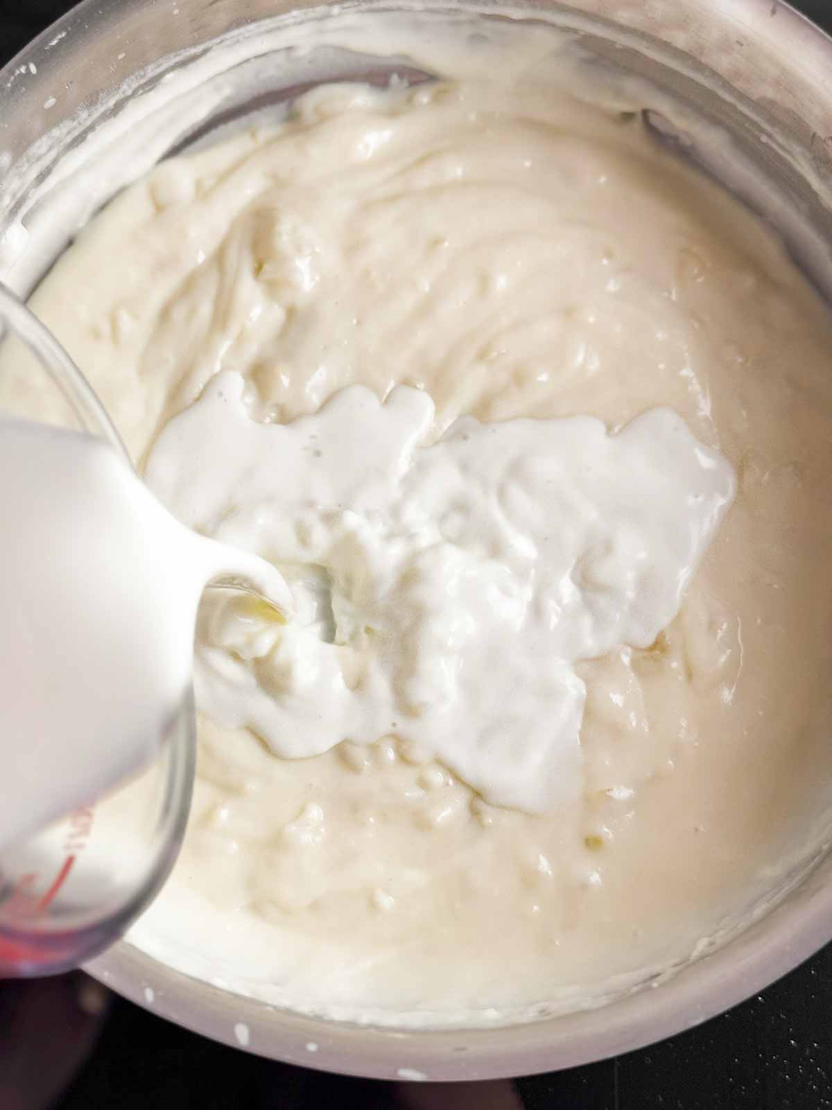 milk pouring from glass measuring jug over white sauce in saucepan