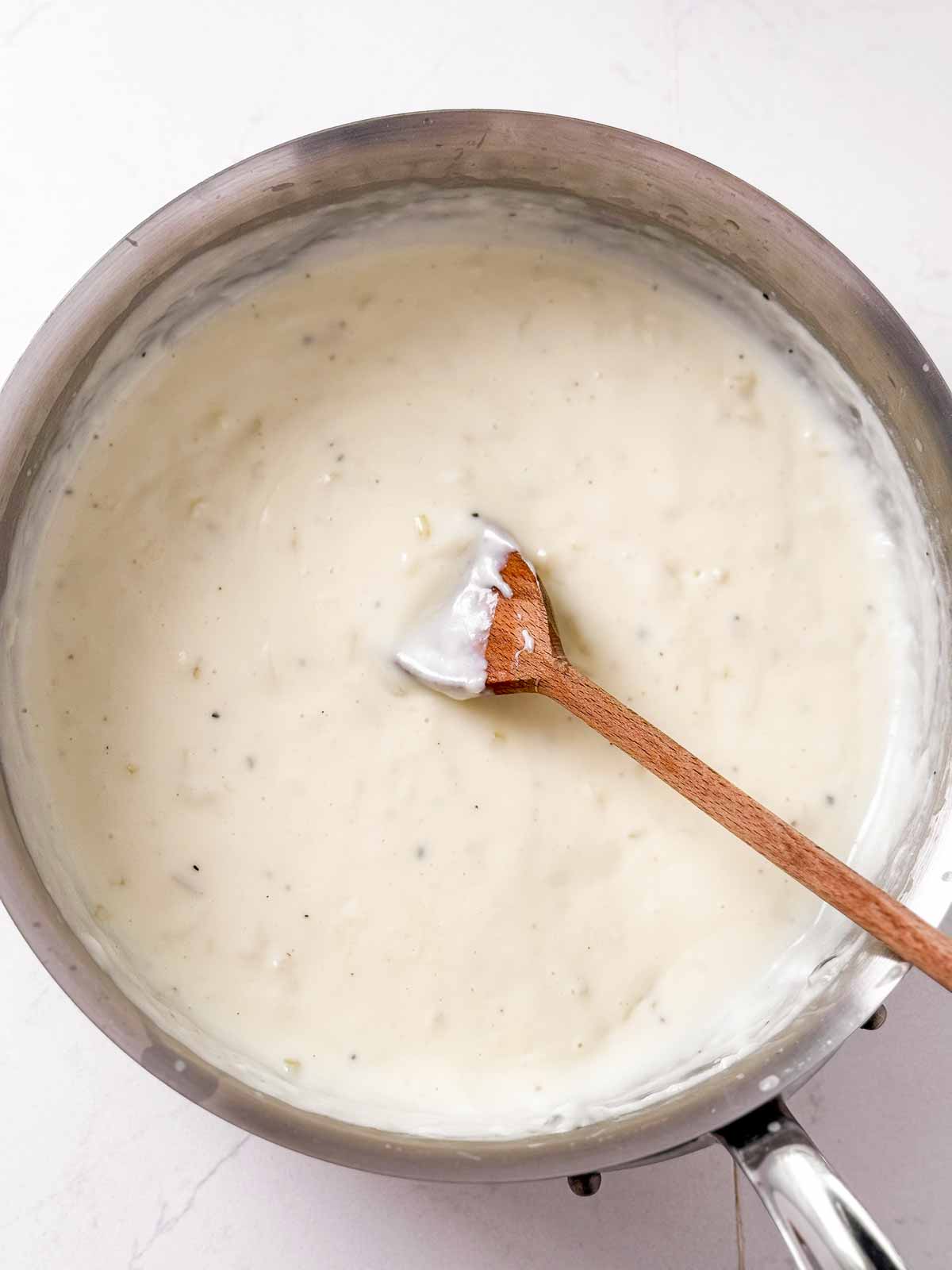 overhead view of béchamel sauce in saucepan with wooden spoon