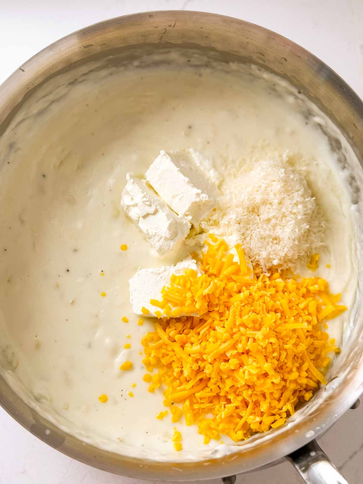 overhead view of shredded cheese and cream cheese in pan with béchamel 