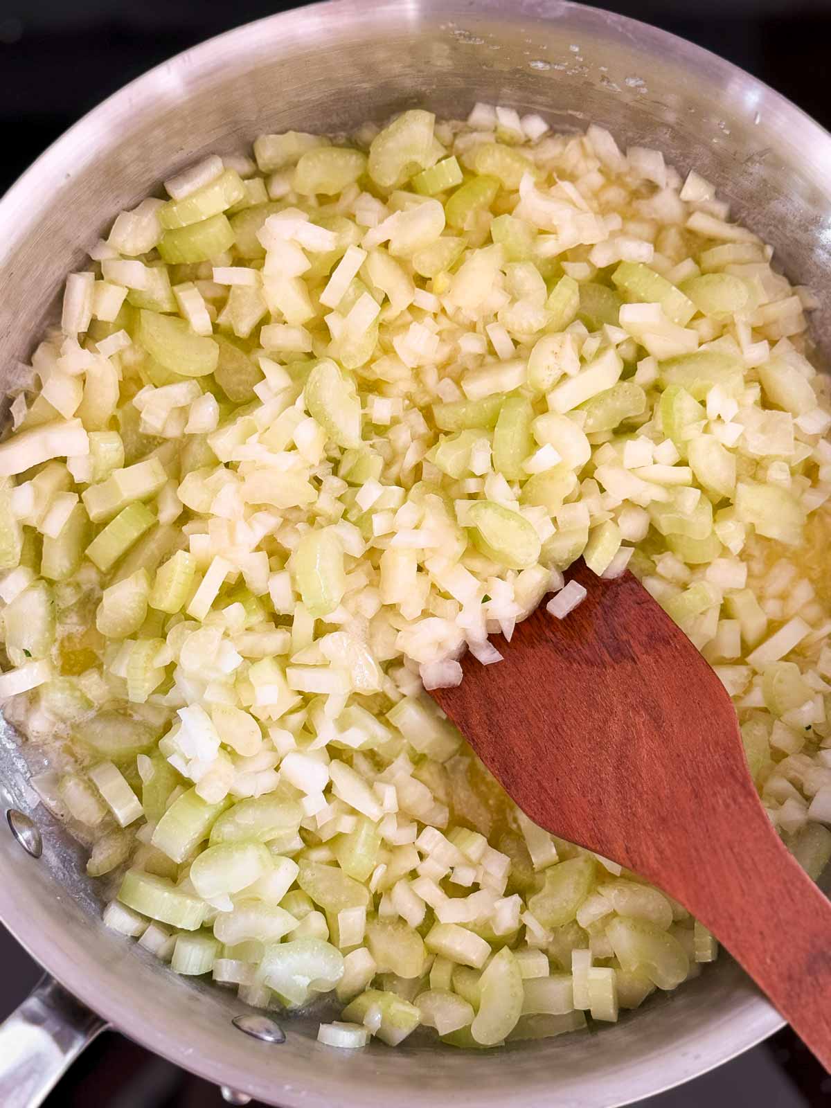 overhead view of uncooked celery and onion in skillet with melted butter and wooden spatula