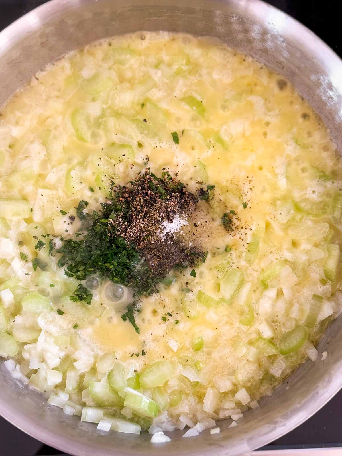 overhead view of cooked celery and onion in skillet with herbs and seasoning