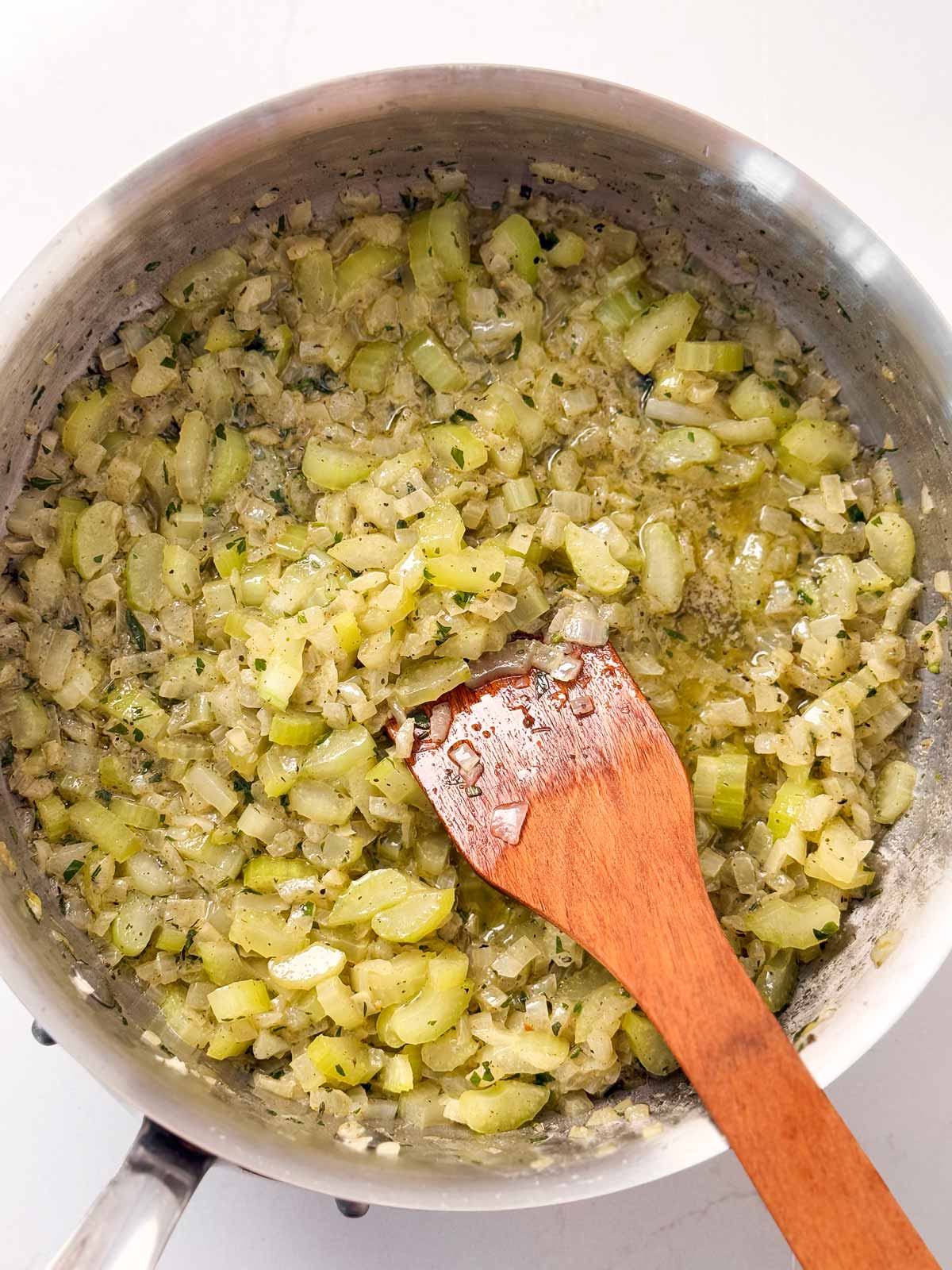 overhead view of cooked celery and onion in skillet with wooden spatula