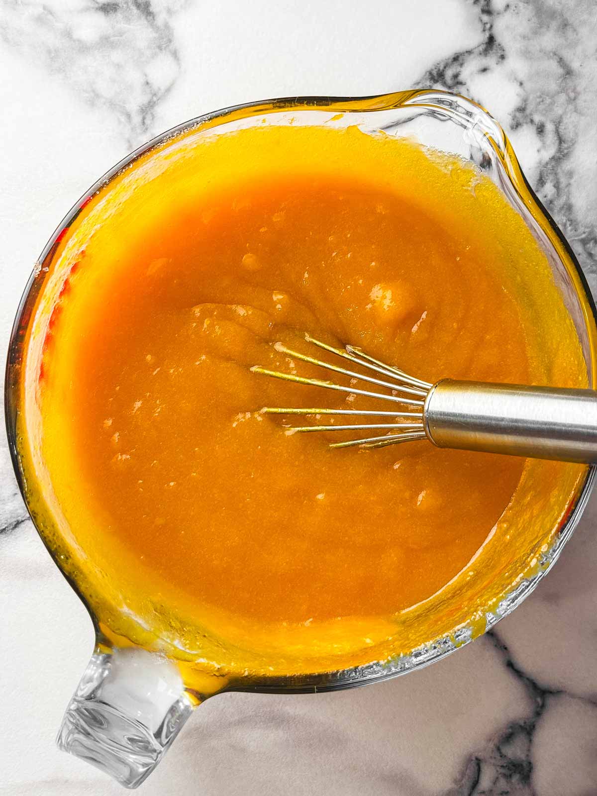 overhead view of wet ingredients for pumpkin bread in glass bowl with whisk