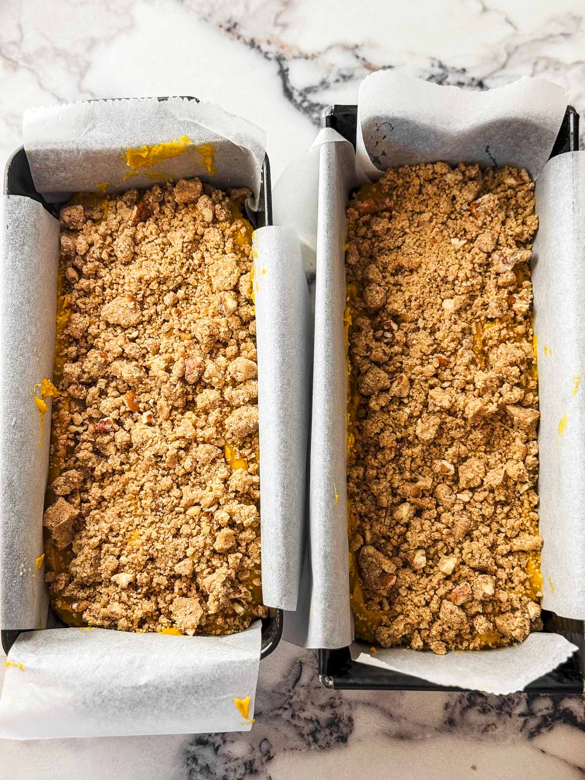 overhead view of pumpkin bread batter topped with streusel in two loaf pans