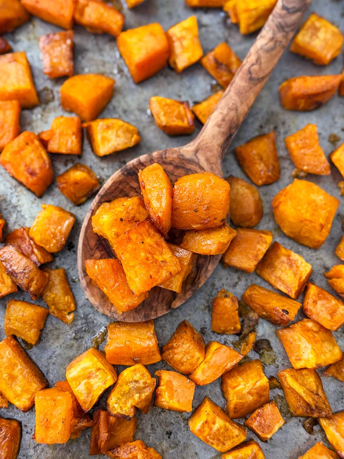 overhead view of roasted sweet potatoes on wooden spoon on top of sheet pan