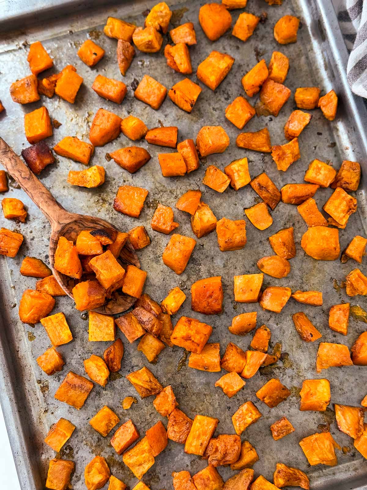 overhead view of roasted sweet potato cubes on sheet pan with wooden spoon