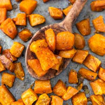 overhead view of roasted sweet potatoes on wooden spoon on top of sheet pan