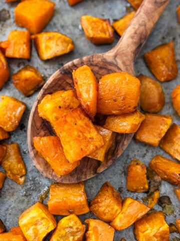 overhead view of roasted sweet potatoes on wooden spoon on top of sheet pan